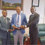 NGL students Harunah Damba (left) and Patrovas Okidi (right) hand over the plaque to Prof. Barnabas Nawangwe (centre).