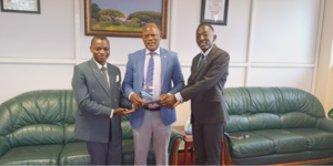 NGL students Harunah Damba (left) and Patrovas Okidi (right) hand over the plaque to Prof. Barnabas Nawangwe (centre).